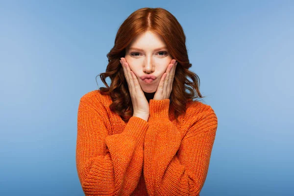 Young redhead woman in orange sweater puffing cheeks isolated on blue — Stock Photo