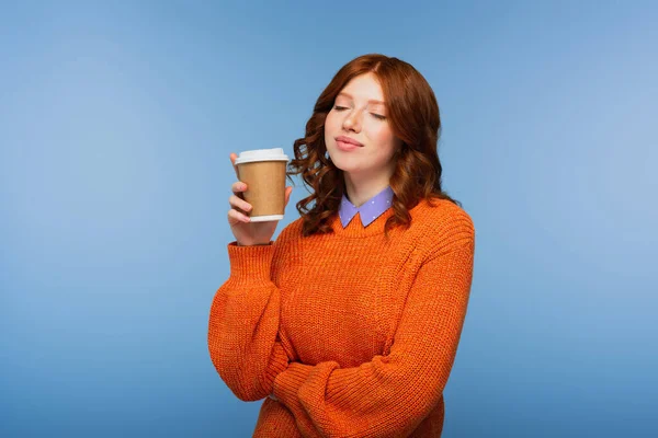 Felice rossa donna in maglione arancione che tiene il caffè per andare isolato sul blu — Foto stock