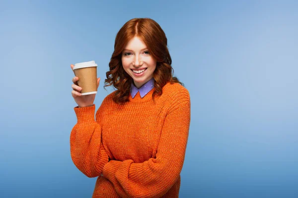 Heureuse rousse femme en pull orange tenant café pour aller isolé sur bleu — Photo de stock