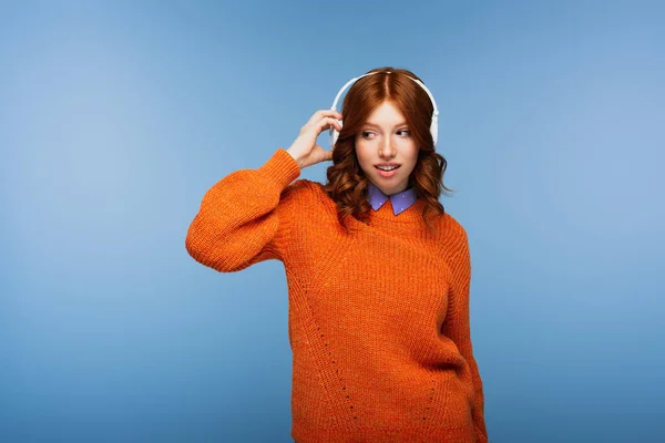 Rothaarige Frau hört Musik in drahtlosen Kopfhörern isoliert auf blau — Stockfoto