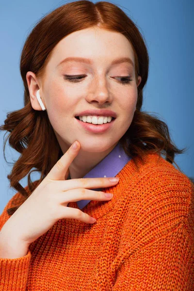 Happy redhead woman listening music in wireless earphones isolated on blue — Stock Photo