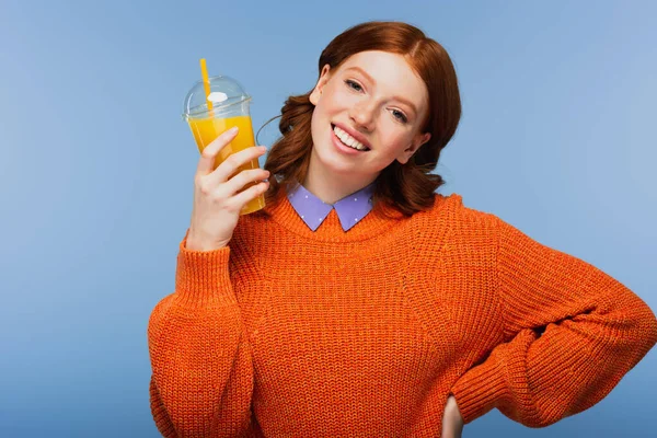 Zufriedene junge Frau im Pullover mit frischem Orangensaft in Plastikbecher auf blauem Grund — Stockfoto