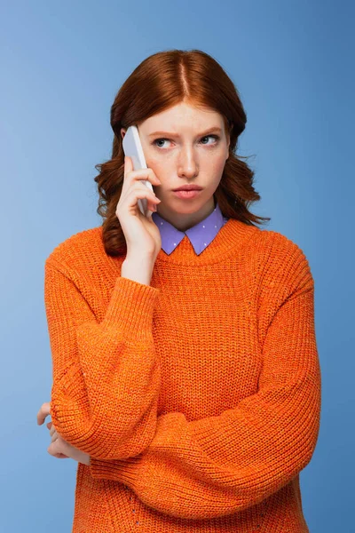 Rothaarige junge Frau in orangefarbenem Pullover unterhält sich auf Smartphone isoliert auf blauem Grund — Stockfoto