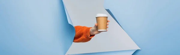 Vista ritagliata di giovane donna in possesso di tazza di carta con caffè per andare su sfondo di carta blu strappato, banner — Foto stock