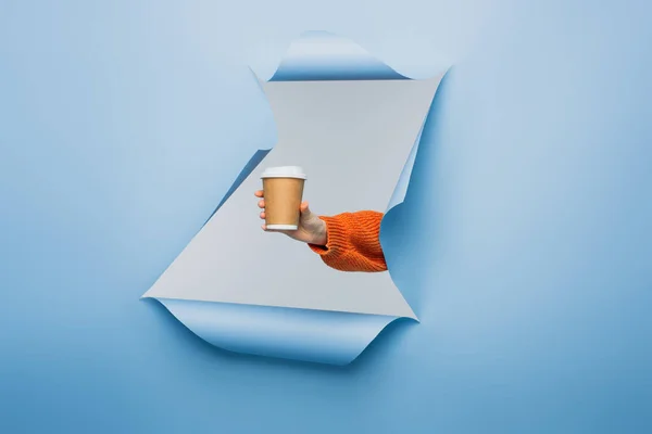 Cropped view of young woman holding paper cup on blue ripped paper background — Stock Photo
