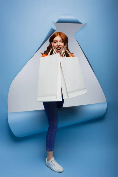 Amazed young woman holding shopping bags on blue ripped paper background — Stock Photo