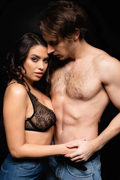 Sexy woman in lace bra holding hands with shirtless man isolated on black — Stock Photo