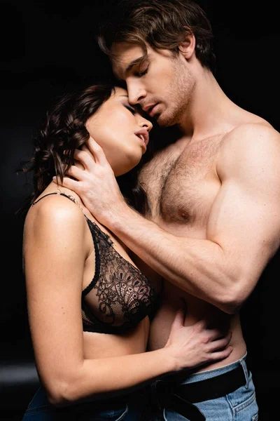 Muscoloso uomo abbracciare seducente bruna donna su nero — Foto stock