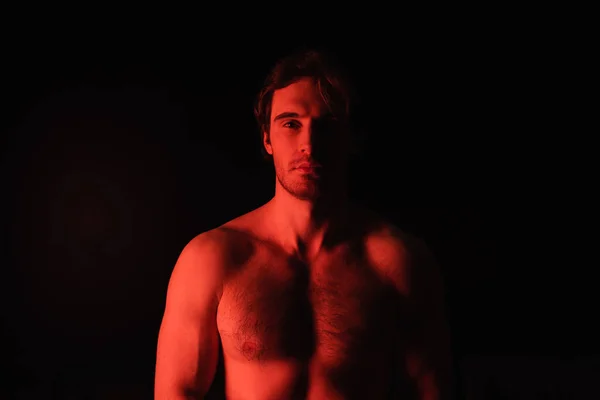 Iluminación roja en el hombre sexy sin camisa mirando a la cámara aislada en negro - foto de stock