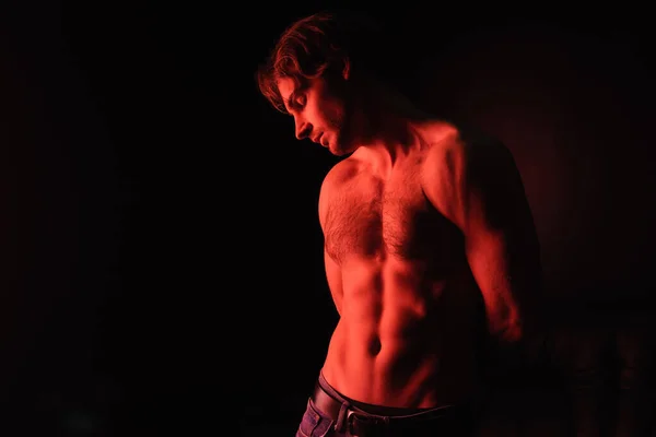 Illuminazione rossa sul corpo dell'uomo muscoloso sexy in piedi isolato sul nero — Foto stock