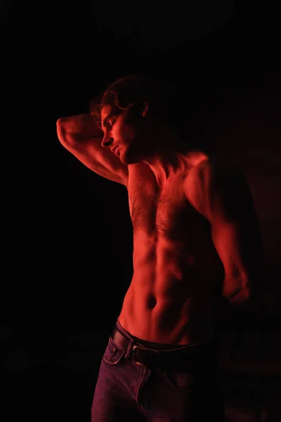 Éclairage rouge sur le corps de l'homme musclé debout isolé sur noir — Photo de stock