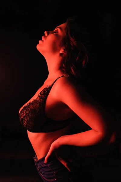 Vista lateral de la mujer sexy en sujetador de encaje de pie aislado en negro - foto de stock