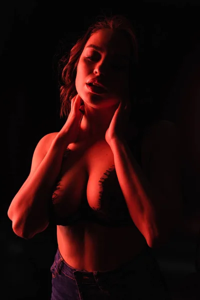 Iluminación roja en la mujer seductora en sujetador de encaje aislado en negro - foto de stock