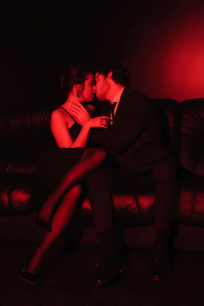 Illuminazione rossa su coppia sexy baciare sul divano in pelle nera — Foto stock