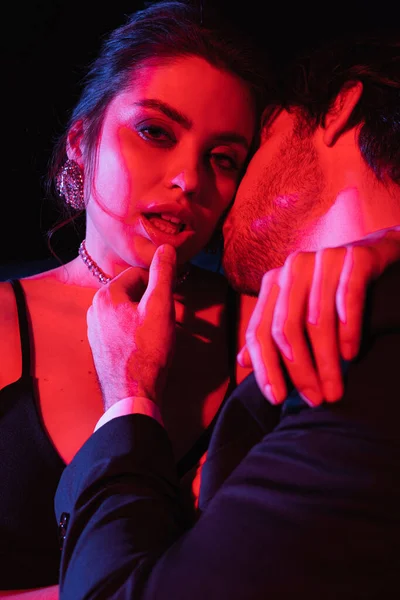 Illuminazione rossa e blu su uomo baciare collo di donna seducente — Foto stock