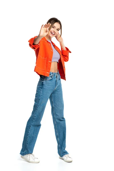 Full length of happy young woman in crop top and orange shirt gesturing isolated on white — Stock Photo