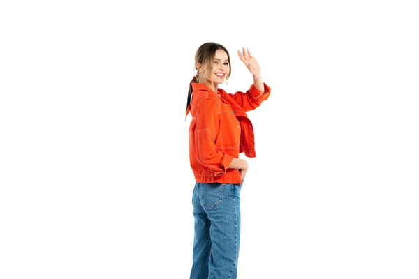 Щаслива молода жінка в джинсах і помаранчевій сорочці махає рукою ізольовано на білому — стокове фото