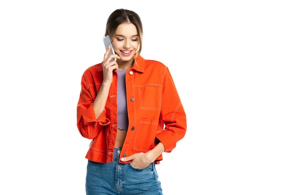 Mujer joven feliz en jeans y camisa naranja hablando en teléfono inteligente aislado en blanco - foto de stock