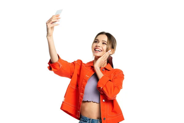 Mujer joven feliz en la parte superior de la cosecha y camisa naranja tomar selfie en el teléfono inteligente aislado en blanco - foto de stock