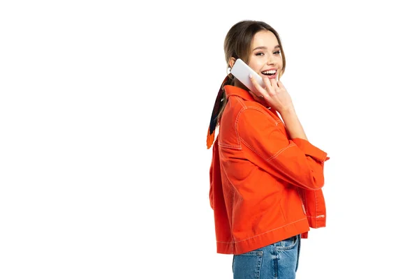 Mujer joven feliz en jeans y camisa naranja hablando en teléfono inteligente aislado en blanco - foto de stock