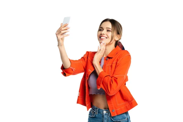 Alegre joven mujer en la parte superior de la cosecha y camisa naranja tomar selfie en el teléfono inteligente aislado en blanco - foto de stock