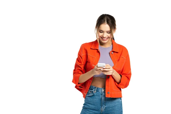 Felice giovane donna in crop top e camicia arancione utilizzando smartphone isolato su bianco — Foto stock