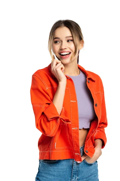 Alegre joven mujer en la parte superior de la cosecha y camisa naranja hablando en el teléfono inteligente aislado en blanco - foto de stock