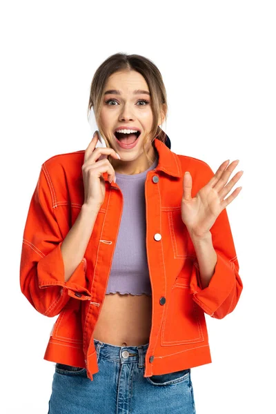 Взволнованная молодая женщина в топе и оранжевой рубашке говорит на смартфоне изолированы на белом — стоковое фото