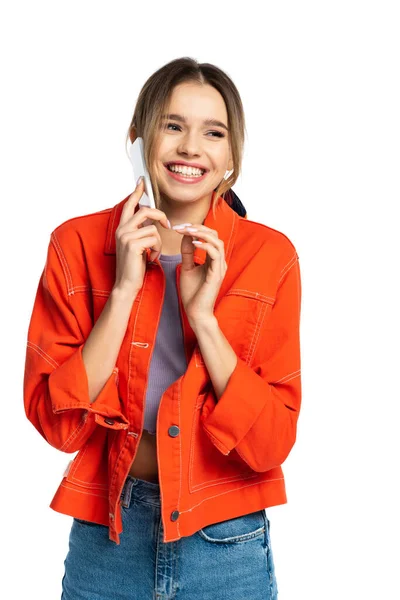 Alegre mujer joven en camisa naranja hablando en teléfono inteligente aislado en blanco - foto de stock