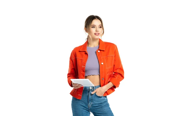 Junge Frau in orangefarbenem Hemd und Jeans mit digitalem Tablet, während sie mit der Hand in der Tasche auf weiß isoliert steht — Stockfoto