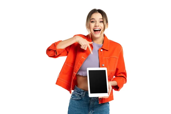 Erstaunt junge Frau in orangefarbenem Hemd und Jeans zeigt auf digitales Tablet mit leerem Bildschirm isoliert auf weißem Hintergrund — Stockfoto