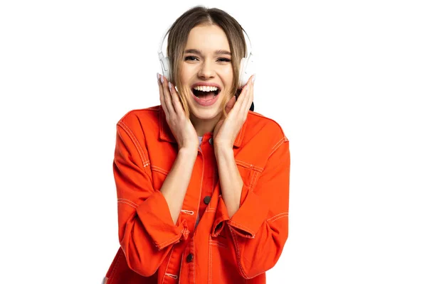 Femme étonnée en chemise orange écouter de la musique dans des écouteurs sans fil isolés sur blanc — Photo de stock