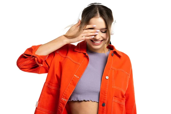 Femme gaie en chemise orange et crop top écouter de la musique dans des écouteurs sans fil isolés sur blanc — Photo de stock