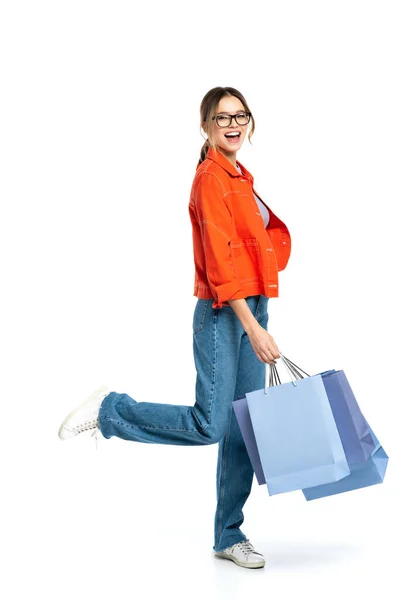 Pleine longueur de femme heureuse en chemise orange tenant des sacs à provisions isolés sur blanc — Photo de stock