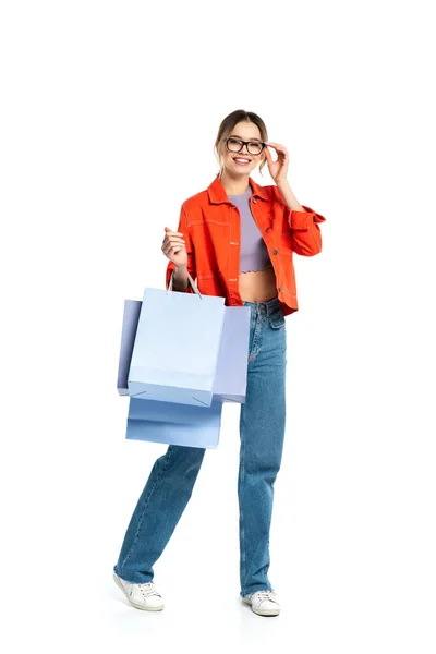 Longitud completa de la mujer sonriente en camisa naranja sosteniendo bolsas de compras aisladas en blanco - foto de stock
