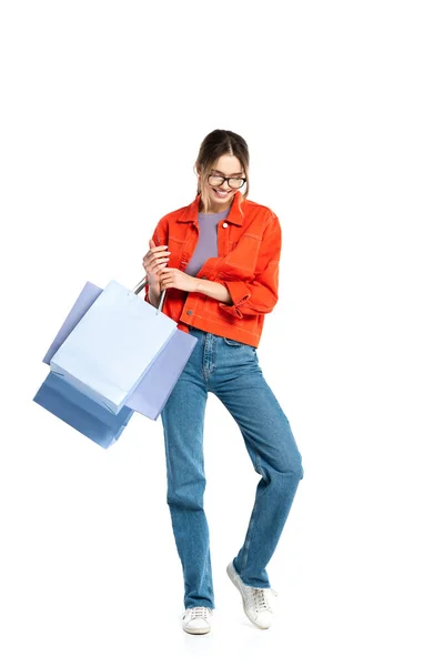 Pleine longueur de femme heureuse en chemise orange tenant des sacs à provisions isolés sur blanc — Photo de stock