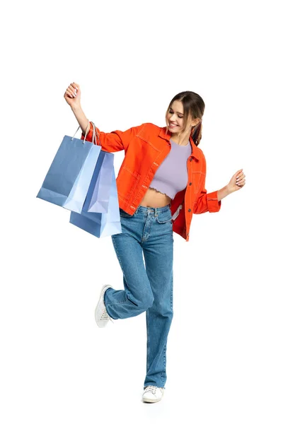 Full length of happy young woman in orange shirt looking at shopping bags isolated on white — Stock Photo