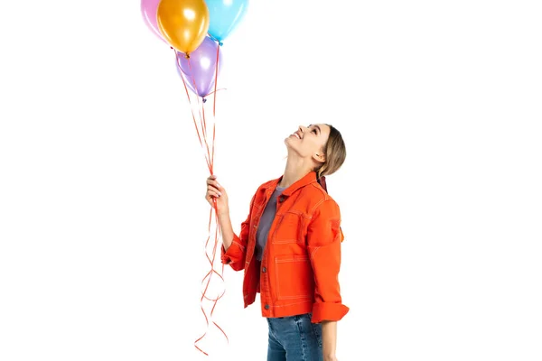 Mujer joven complacida en camisa naranja mirando globos de colores aislados en blanco - foto de stock