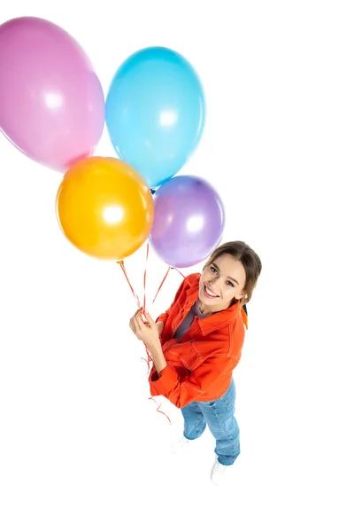 High angle view of happy young woman in orange shirt holding colorful balloons isolated on white — Stock Photo
