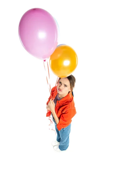 Високий кут зору сумної молодої жінки в помаранчевій сорочці, що тримає барвисті кульки ізольовані на білому — стокове фото