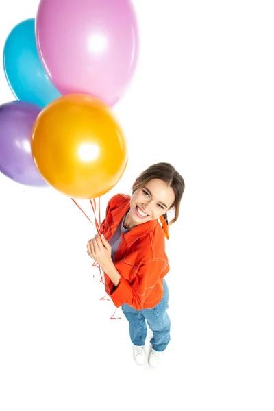 Vista de ángulo alto de la joven sonriente en camisa naranja sosteniendo globos de colores aislados en blanco - foto de stock