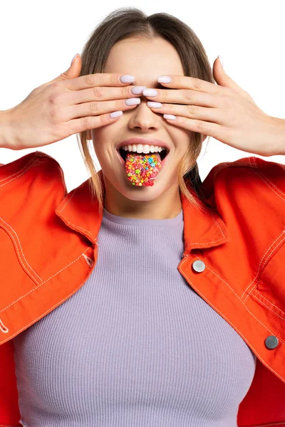 Mujer joven cubriendo los ojos con las manos y sacando la lengua con aspersiones aisladas en blanco - foto de stock