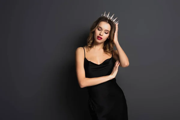 Mujer joven en vestido negro deslizante ajustando tiara con diamantes en gris - foto de stock