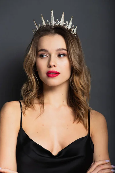 Young woman in black slip dress and tiara with diamonds looking away on grey — Stock Photo
