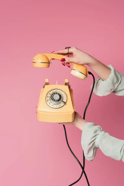 Vista ritagliata di donna che tiene telefono vintage e portatile isolato su rosa — Foto stock