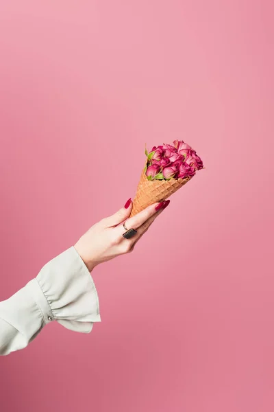 Vista cortada de mulher segurando cone de waffle com flores de rosa isolado em rosa — Fotografia de Stock