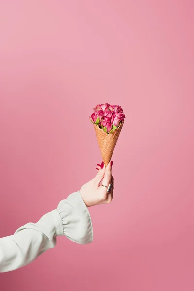 Vista parcial de la mujer sosteniendo delicioso cono de gofre con rosas aisladas en rosa - foto de stock