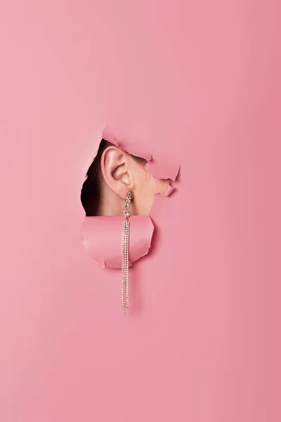 Cropped view of woman in earring near pink background with hole — Stock Photo