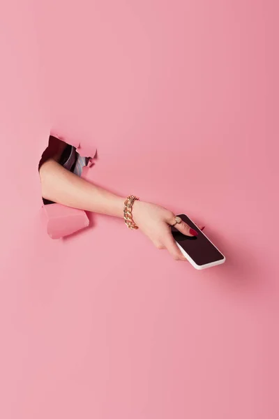 Vue recadrée du smartphone en main de la femme près de fond rose avec trou — Photo de stock