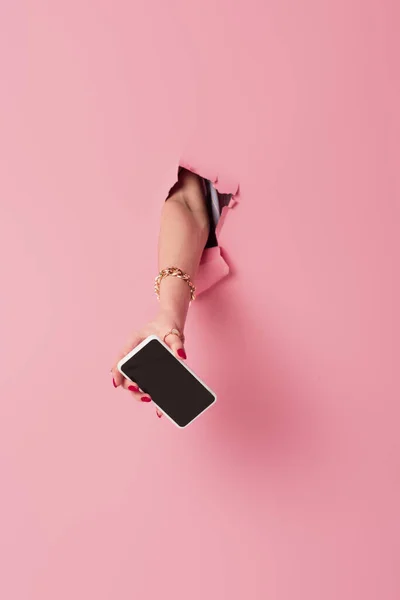 Vue recadrée du smartphone avec écran vierge à la main de la femme près de fond rose avec trou — Photo de stock